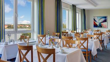 A dining area with tables set for service, large windows with curtains, and a view of the landscape.