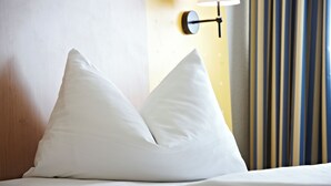 A bed with two white pillows and a wall-mounted lamp. - IntercityHotel Stralsund (Stralsund)