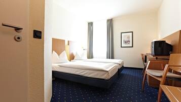 Habitación de hotel con cama, escritorio, silla, televisor y un cuadro en la pared.