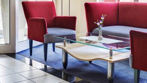 A modern hotel lobby with a red sofa set, a glass coffee table, and a potted plant. - IntercityHotel Stralsund (Stralsund)