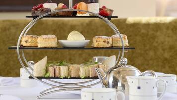 Un présentoir à trois niveaux, garni de diverses pâtisseries et surmonté d’un bol de crème glacée, accompagné de théières et de tasses, le tout disposé sur une table.