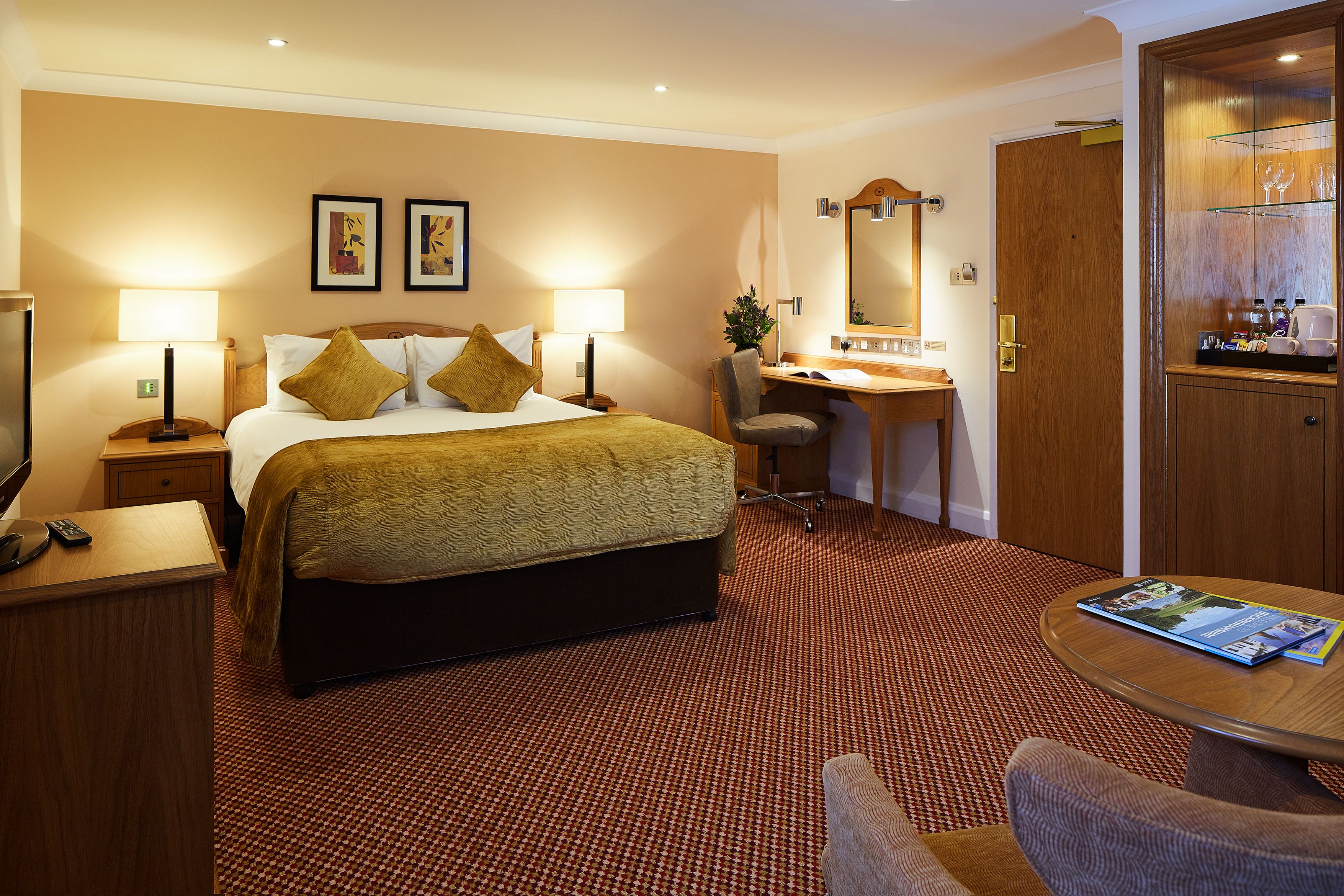A hotel room with a bed, desk, chair, and a table with magazines.