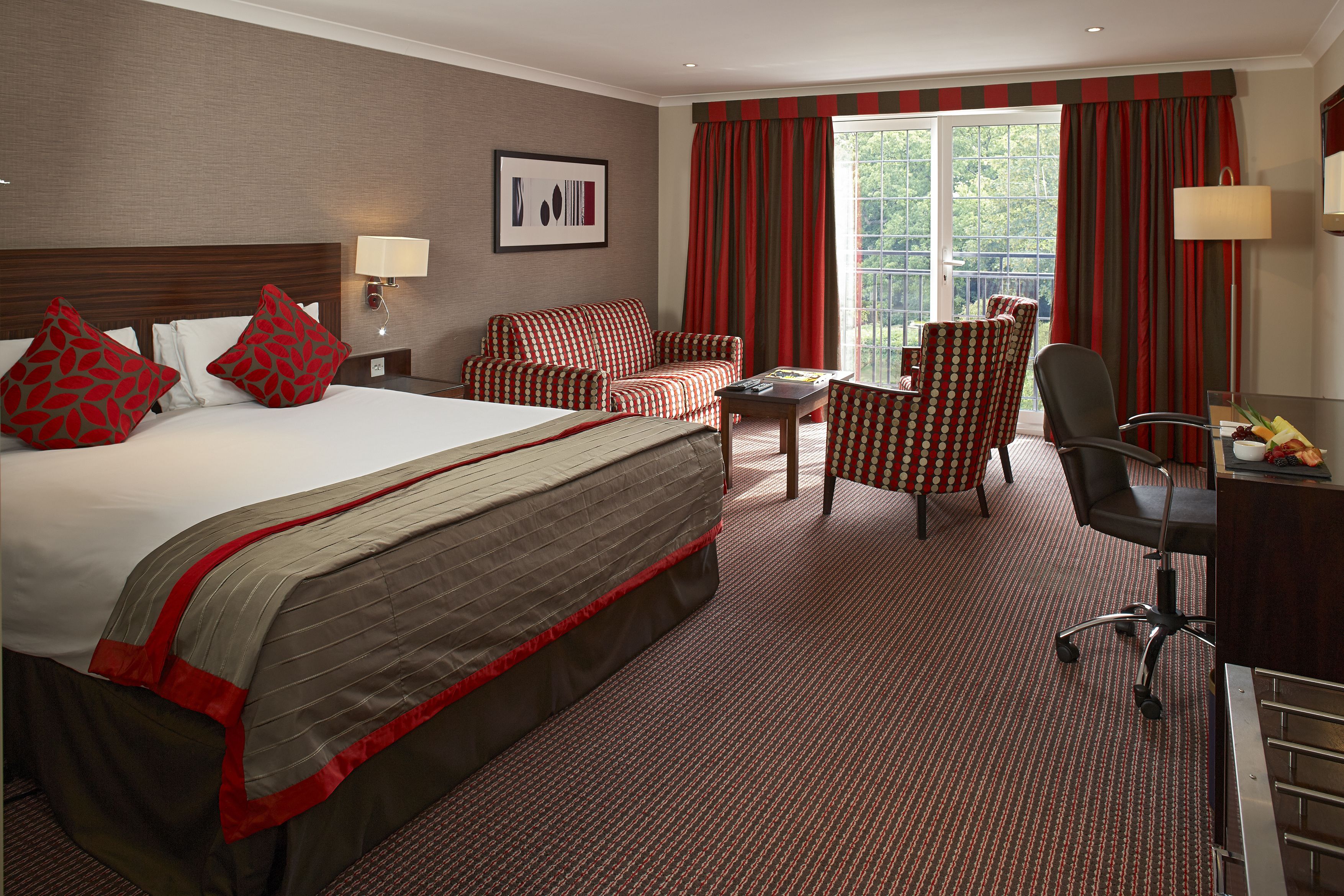 Ein Hotelzimmer mit einem großen Bett, einem Schreibtisch, zwei Stühlen und einem Vorhangfenster.
