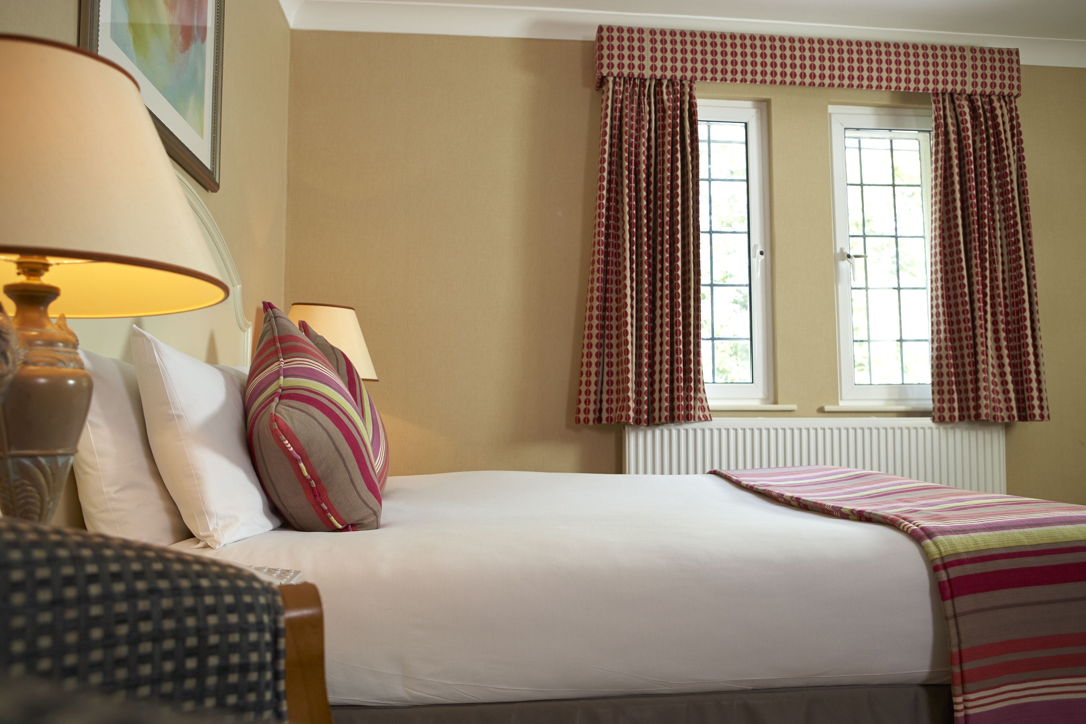 A neatly arranged hotel room with a bed, two bedside lamps, a window with curtains, and a radiator.