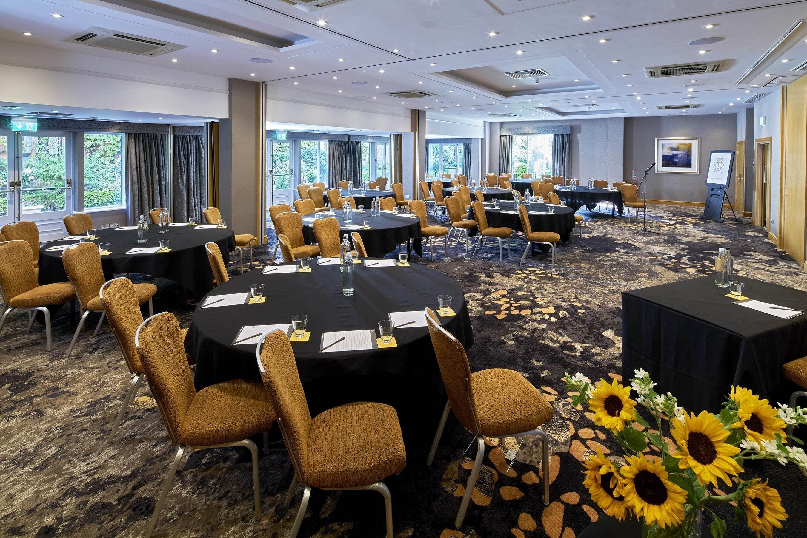 A conference room with multiple round tables, chairs, and a carpeted floor.