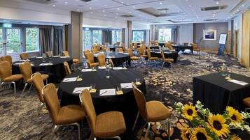 A conference room with multiple round tables, chairs, and a carpeted floor.