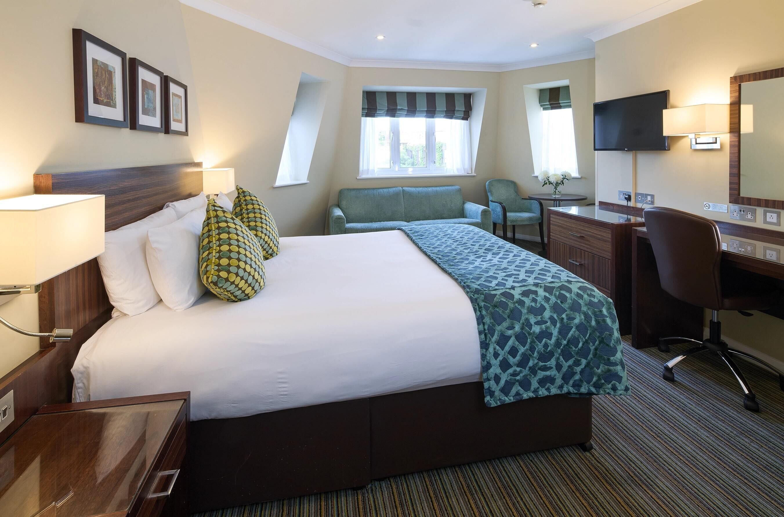 A hotel room with a large bed, a desk, a chair, a television, and a window with curtains.