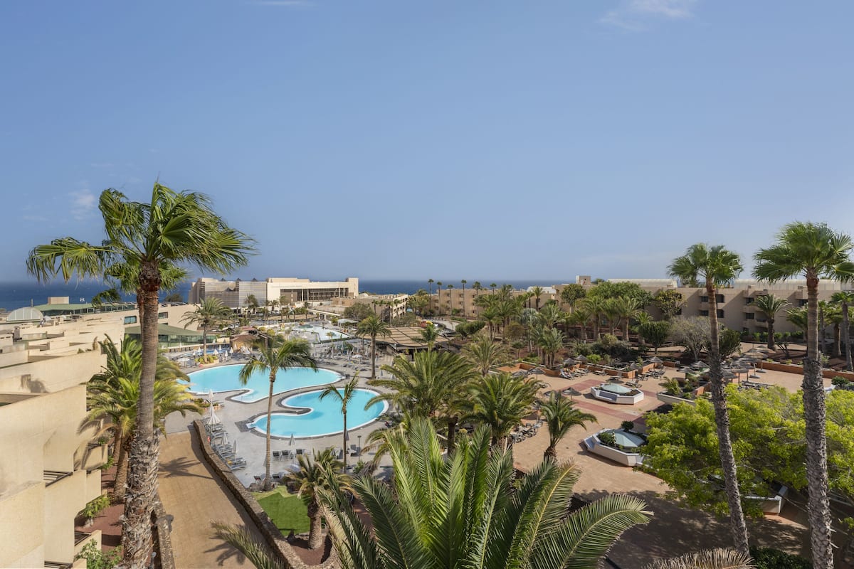 Un resort con una piscina grande, palmeras y vistas al mar.