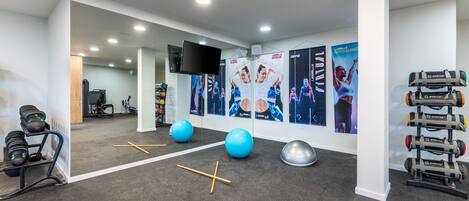 A modern gym with exercise equipment, posters, and a large mirror.