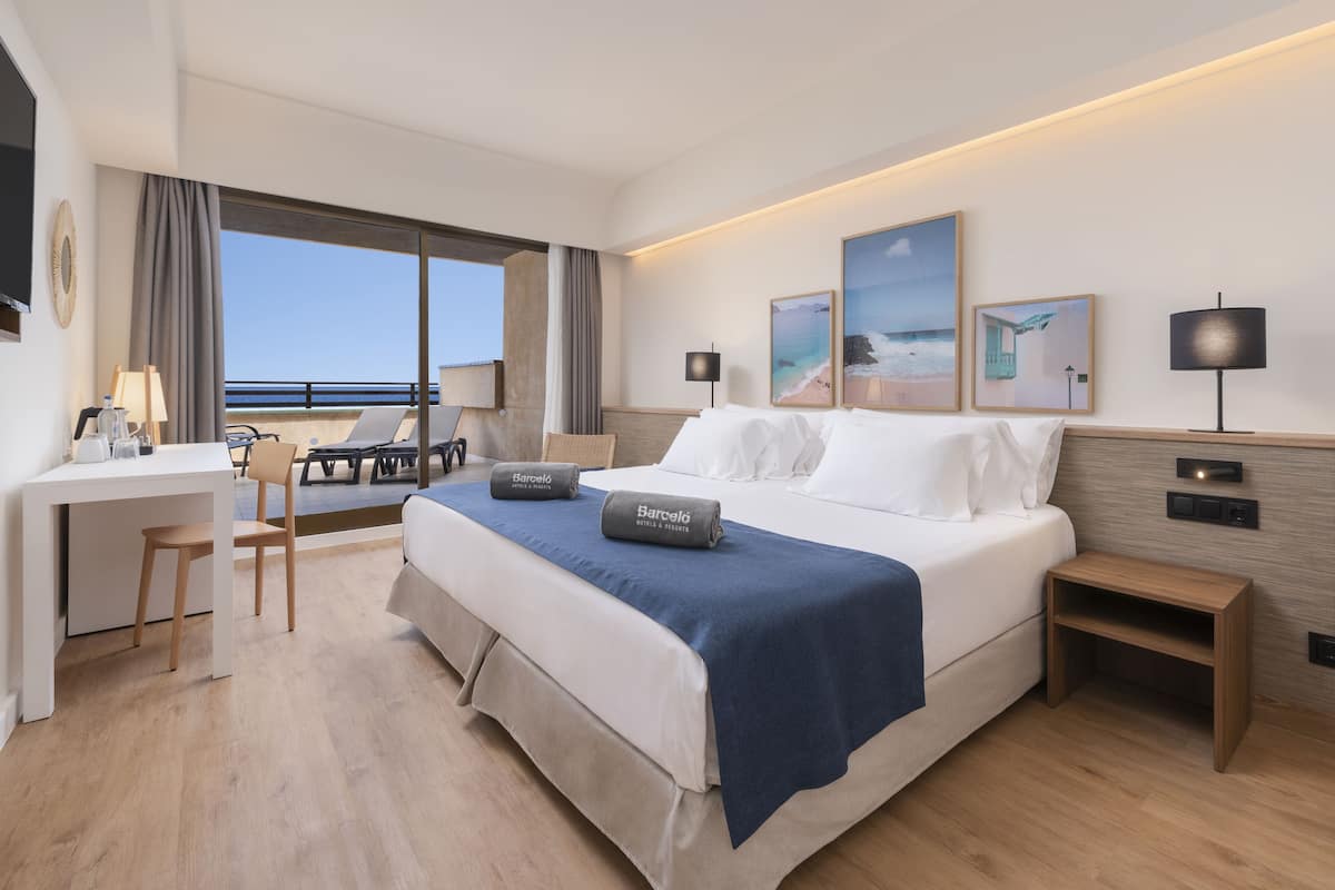 Una habitación de hotel con una cama grande, un escritorio, una silla y vistas al mar.