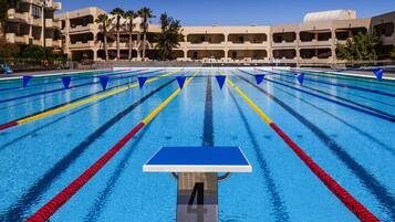 A swimming pool with lane dividers, a starting block labeled '4', and a building with multiple balconies in the background.