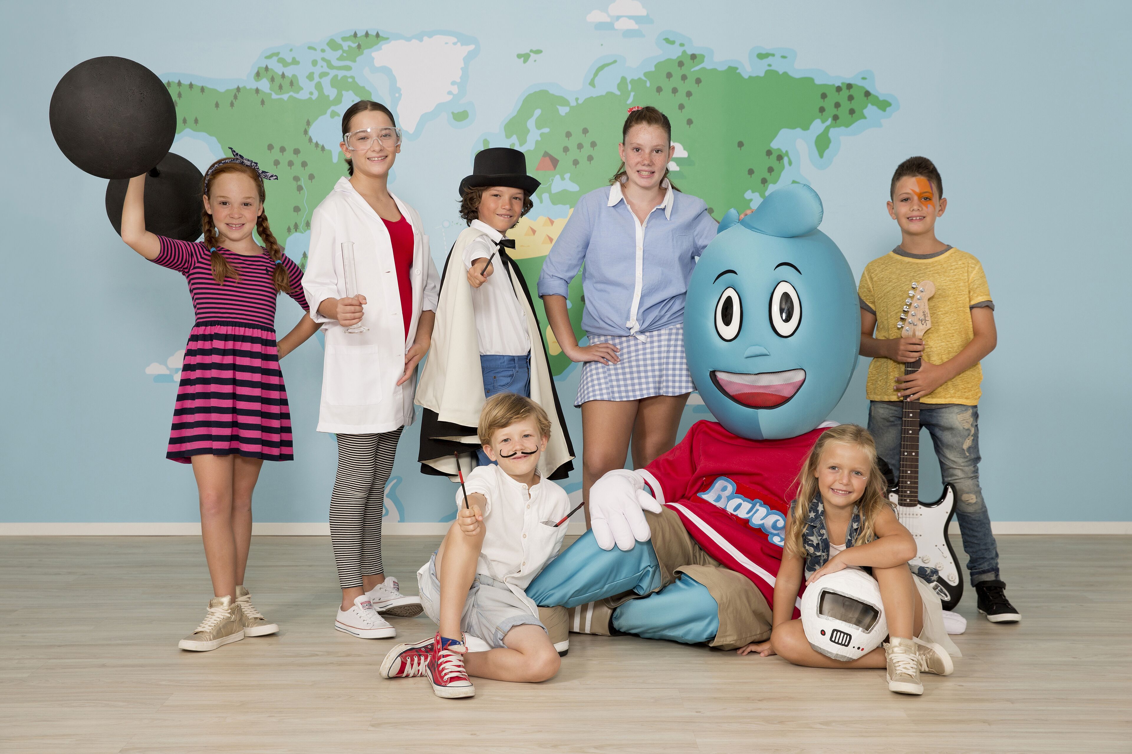 Eine Gruppe Kinder und eine Maskottchenfigur in einem Raum mit einer Weltkarte an der Wand.