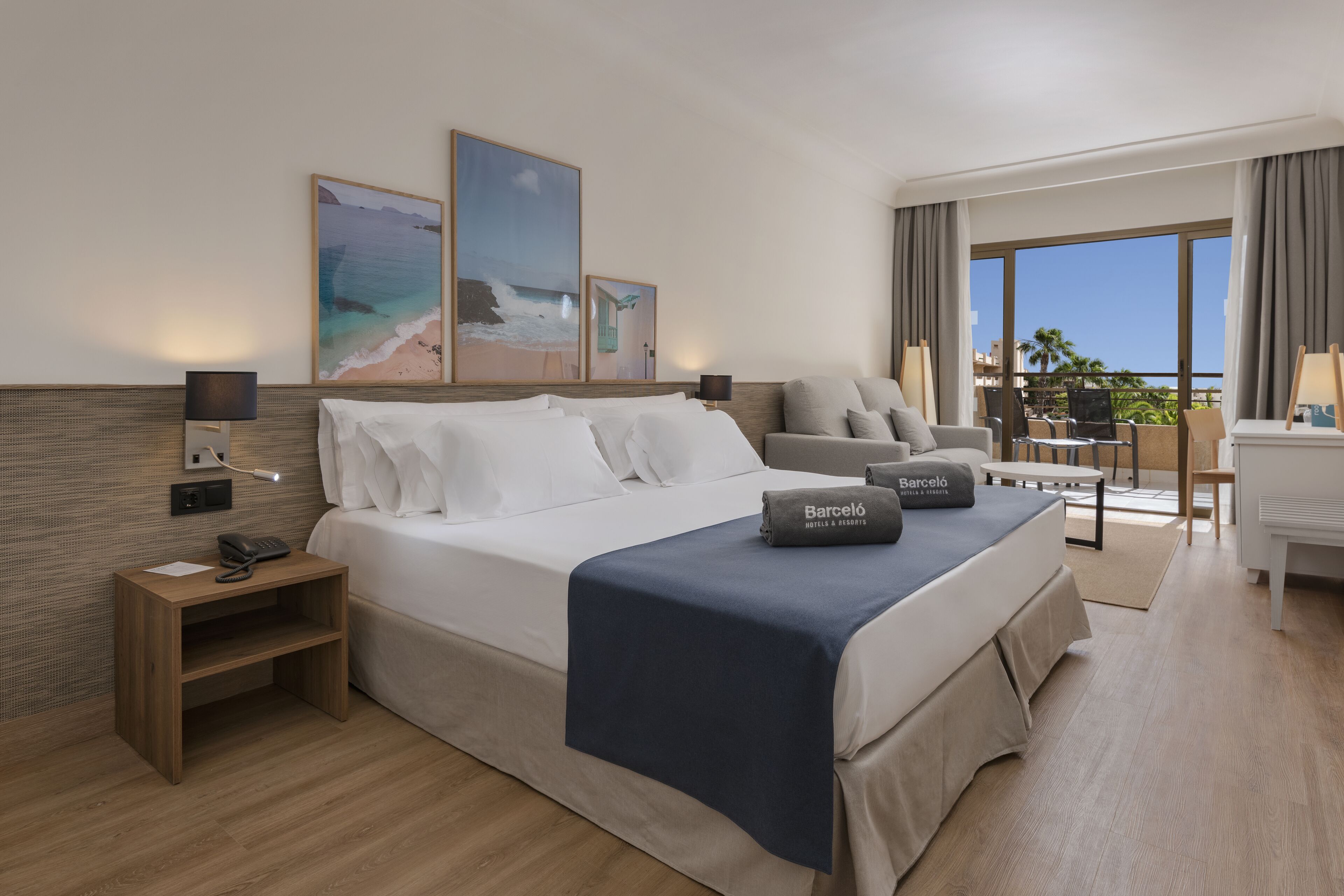 A hotel room with a bed, bedside table, lamp, and a view of the ocean through large windows.