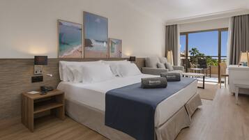 A hotel room with a bed, bedside table, lamp, and a view of the ocean through large windows.