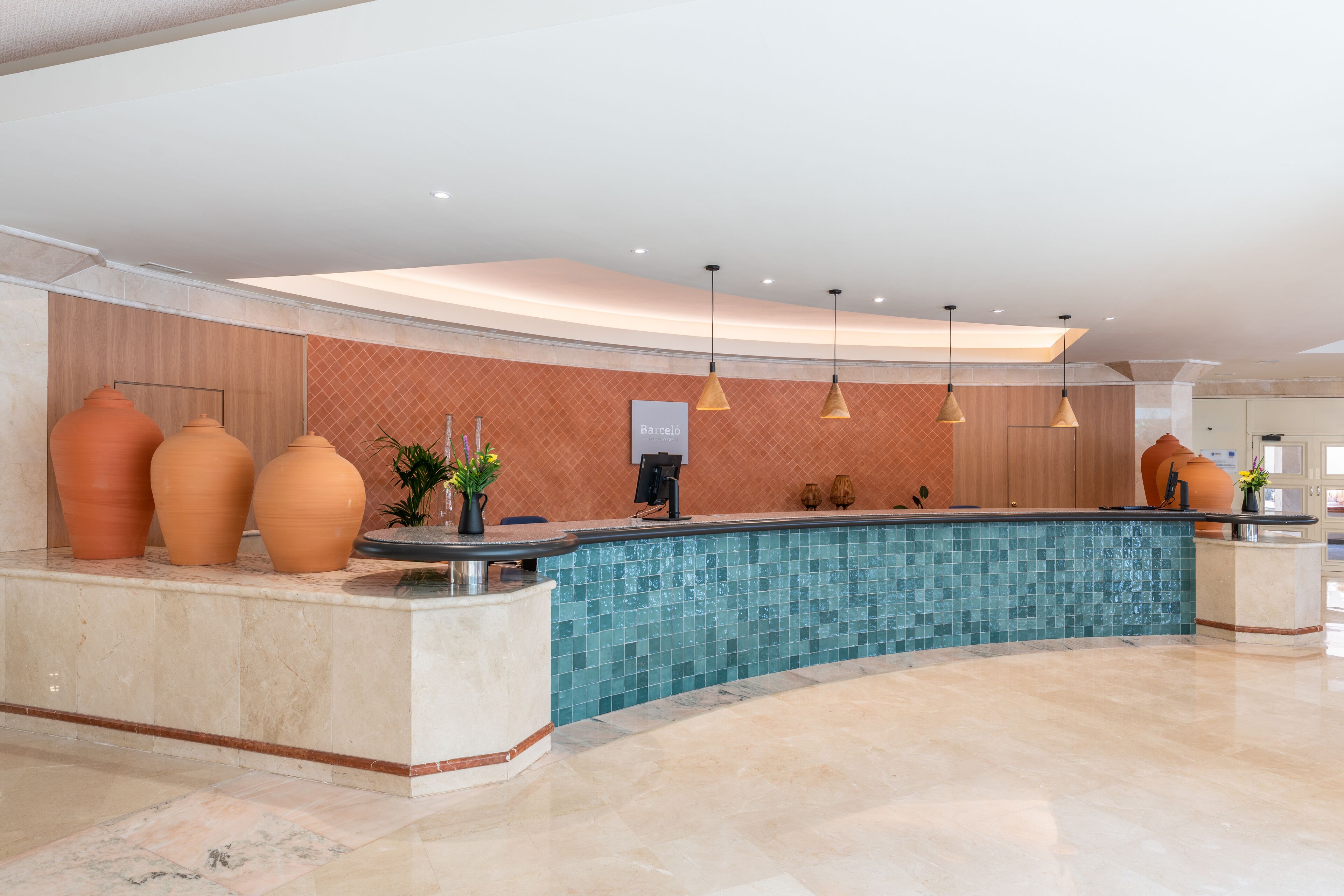 A reception area with a curved marble counter, a tiled pool, and a wooden wall with a 'Barceló' sign.