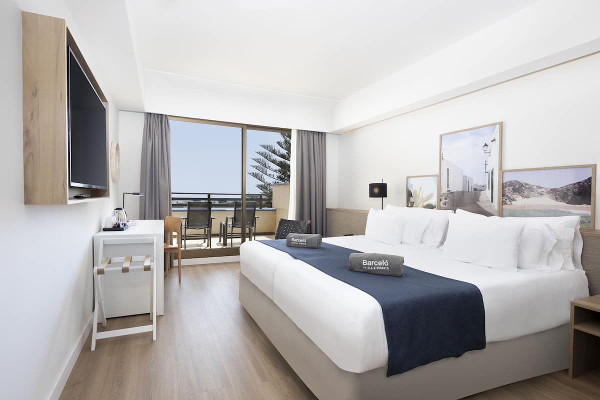 Una habitación de hotel moderna con una cama grande, un escritorio y un balcón con vista al mar.