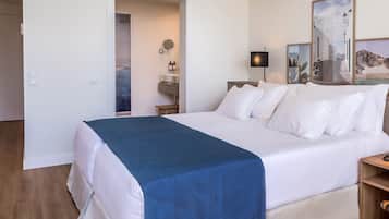 Habitación de hotel con una cama grande, una mesita de noche, una lámpara, un espejo, un lavamanos y una ducha.