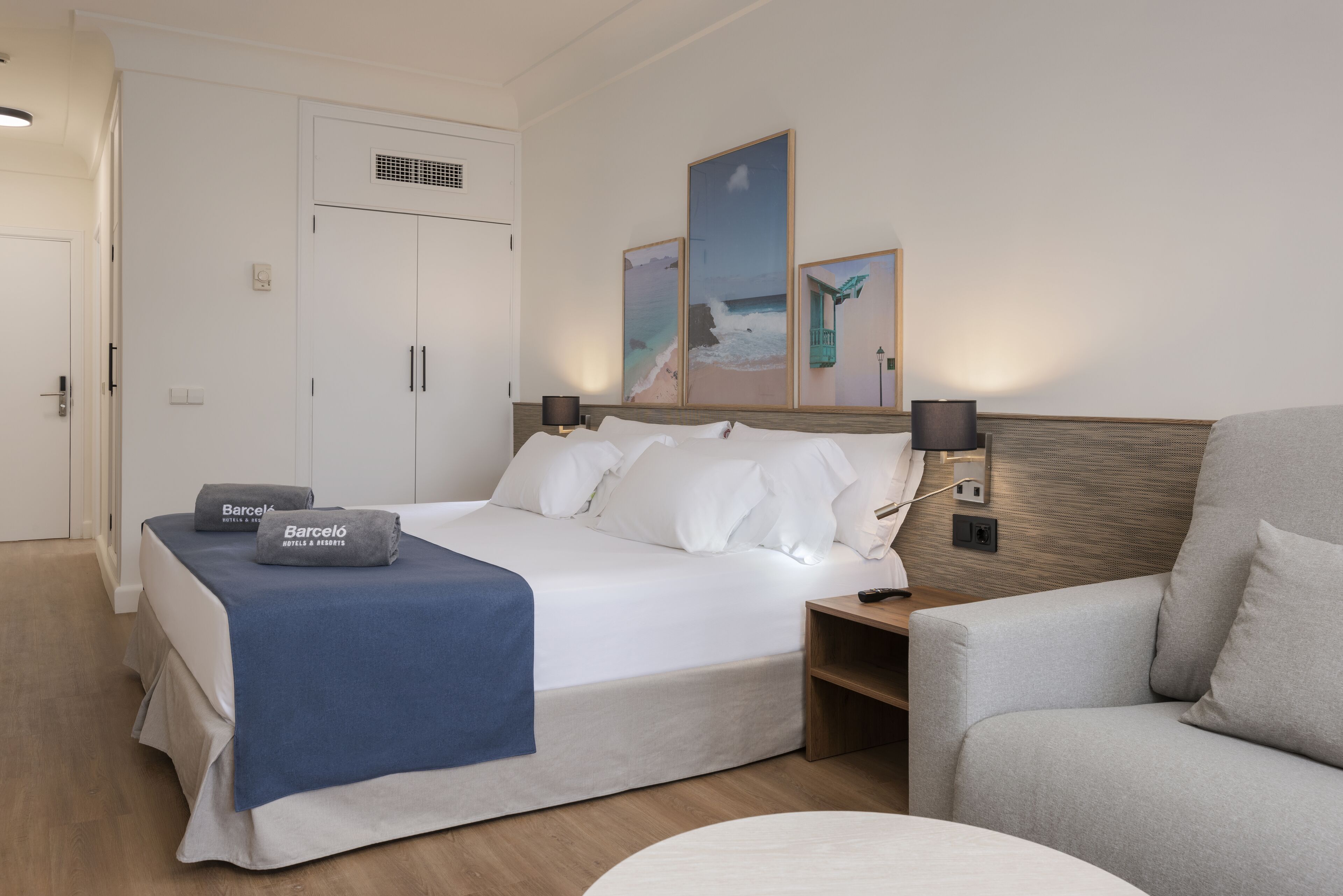 Una habitación de hotel con cama, una silla, una mesita de noche y obras de arte en la pared.