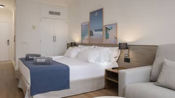 Una habitación de hotel con cama, una silla, una mesita de noche y obras de arte en la pared.