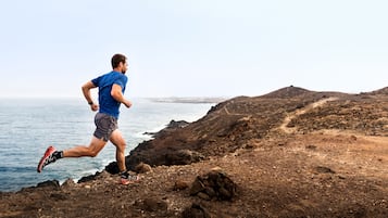A man running along a rocky coastal path with a view of the sea and distant hills.