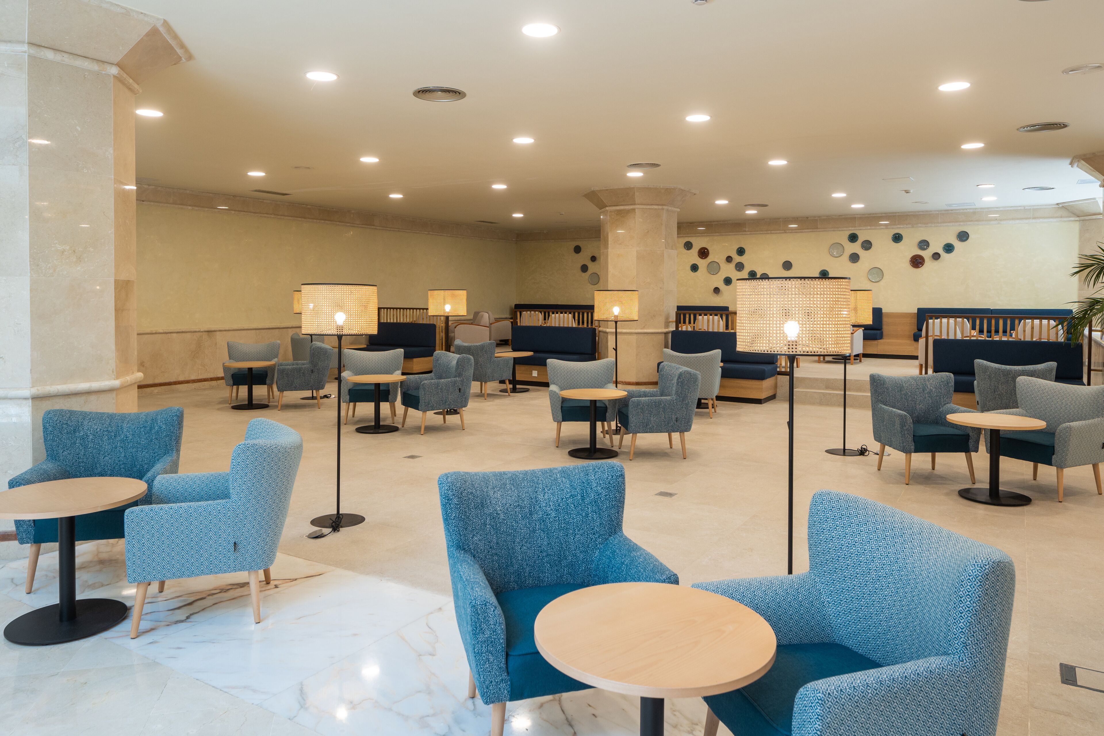 A lobby with blue armchairs and round tables, a column, and wall decor.