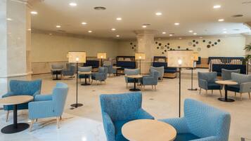 A lobby with blue armchairs and round tables, a column, and wall decor.
