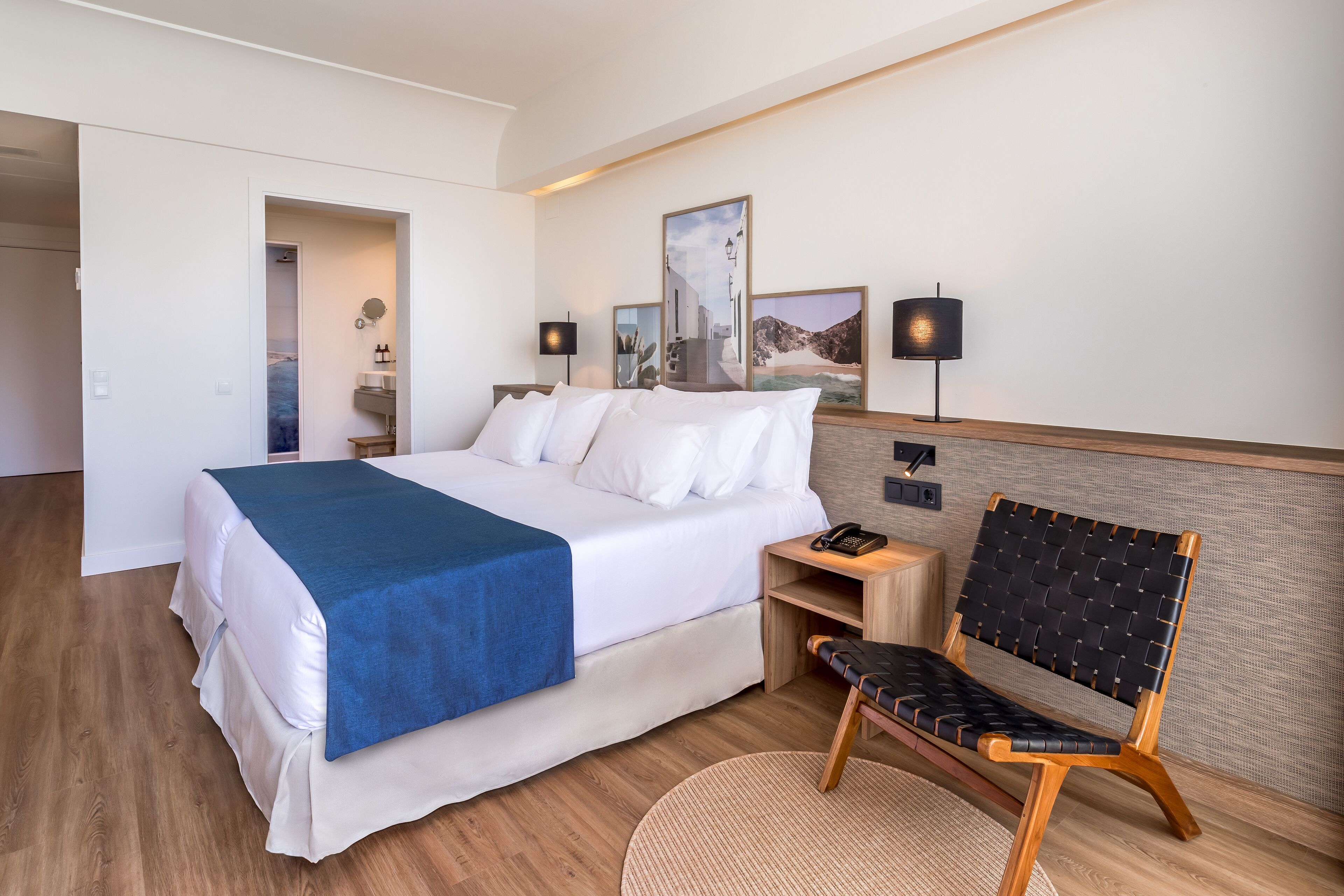 Une chambre d’hôtel avec un grand lit, une table de chevet en bois, une chaise et un téléphone fixé au mur.