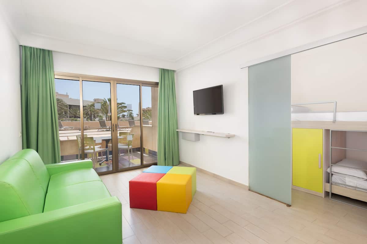 Una habitación moderna con un sofá verde, un bloque de colores, un televisor y una cama alta.