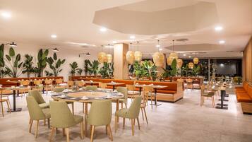 Un vaste espace dédié à la salle à manger, avec des tables rondes, des sièges confortables et des luminaires suspendus.