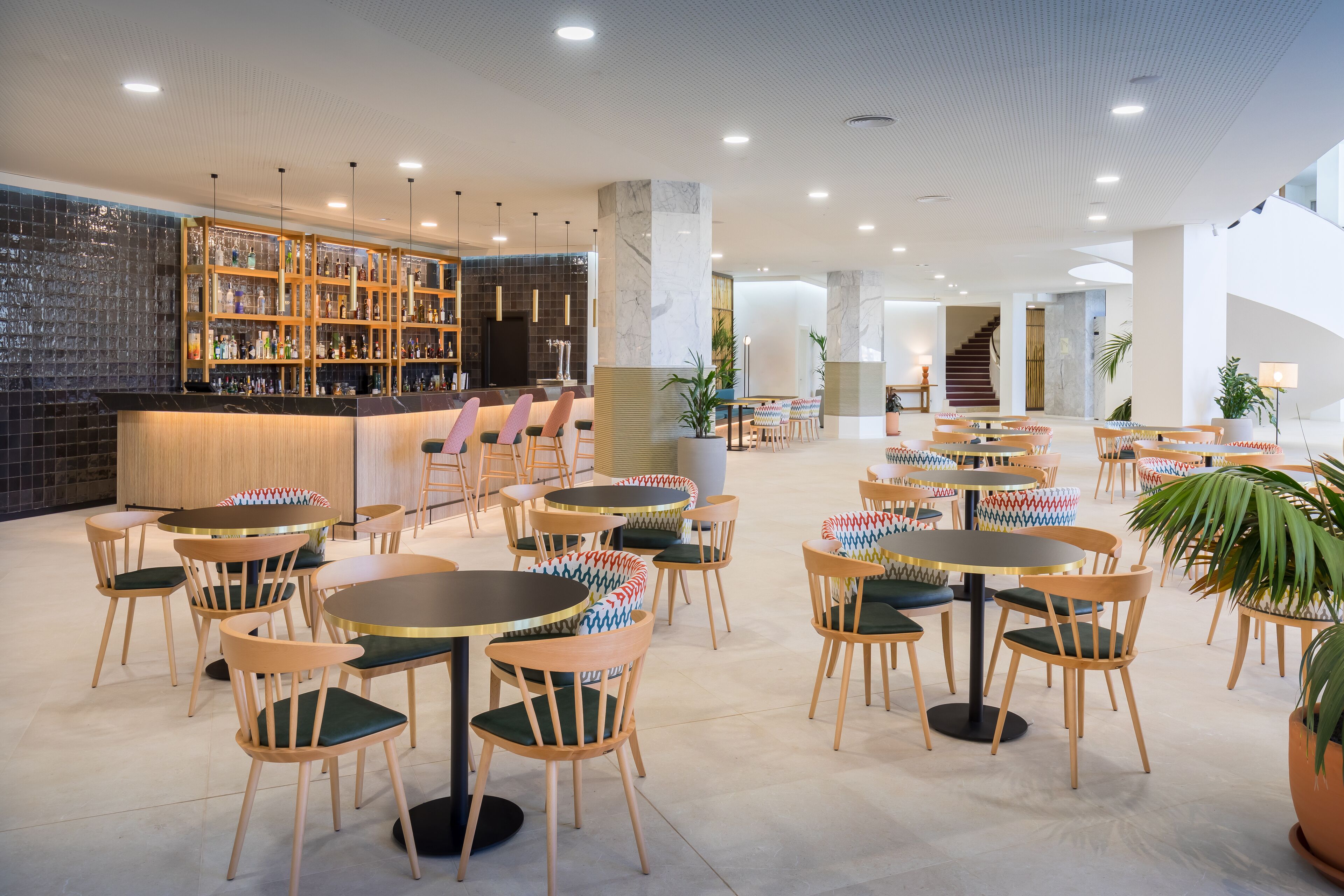 Eine moderne Bar mit gefliestem Rückspritzguss, Holzböden und verschiedenen Sitzgelegenheiten, darunter runde Tische und Stühle.