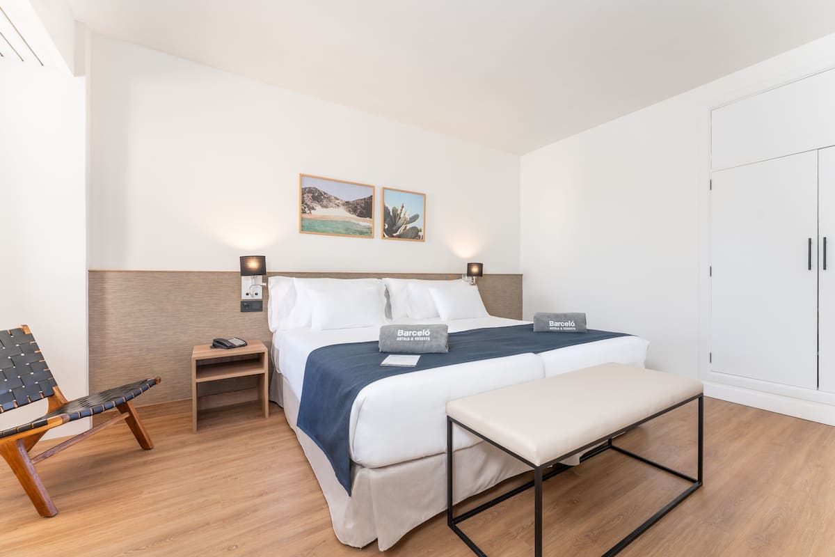 Una habitación de hotel con una cama, mesitas de noche, un banco y un armario.