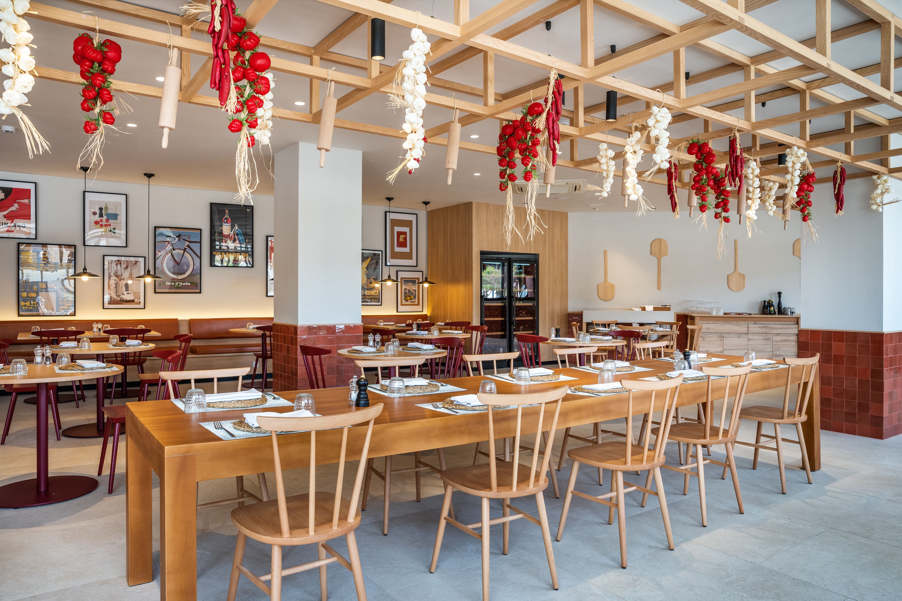 Un restaurant avec des tables et des chaises en bois, des décorations florales suspendues, des œuvres d’art encadrées aux murs et une cuisine ouverte.
