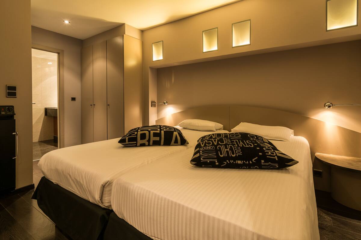 Habitación de hotel con una cama grande, dos mesitas de noche, un armario y un baño visible a través de una puerta abierta.
