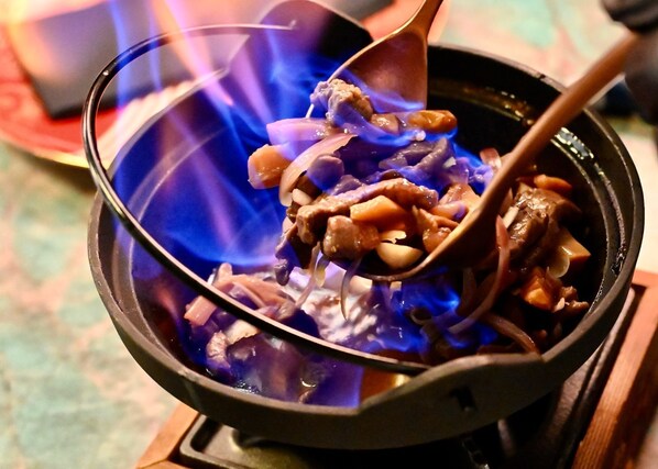 A close-up of a hot pot with various ingredients being stirred over a blue flame. - De Keyser Hotel (Antwerp)