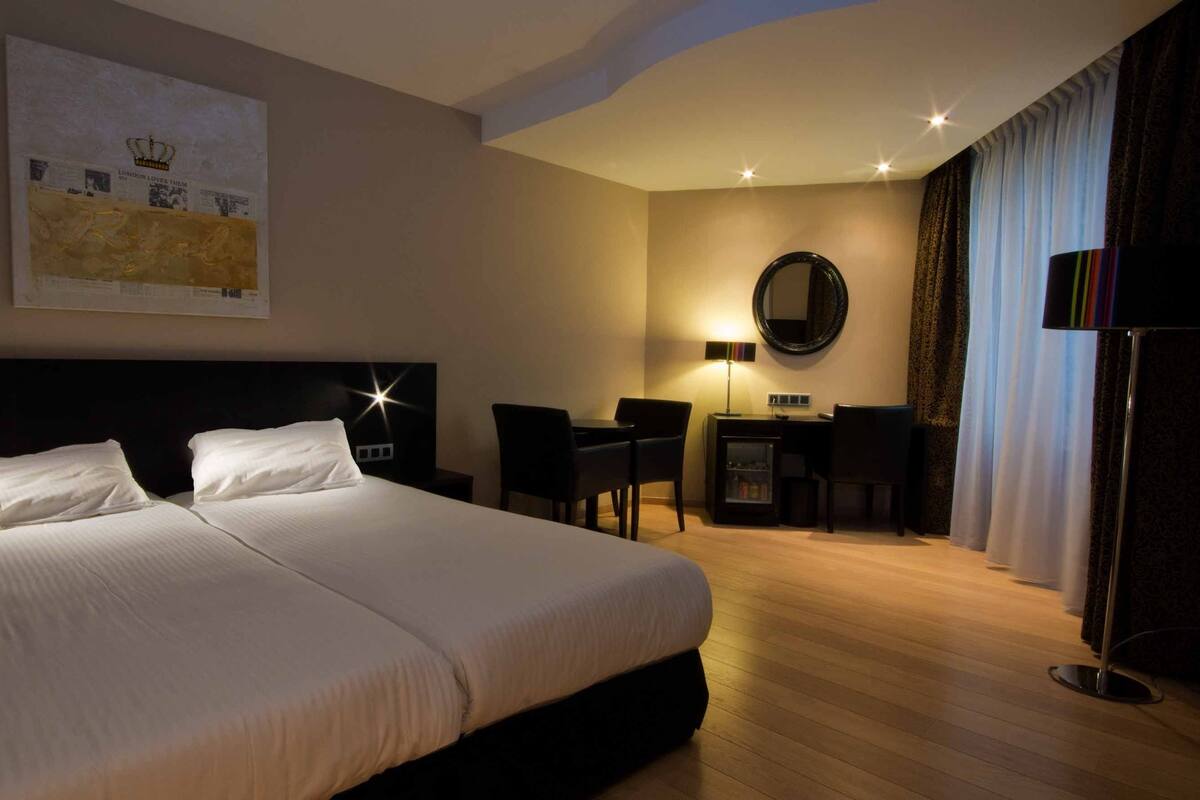 Habitación de hotel con una cama grande, un escritorio, una silla, un espejo y un televisor.