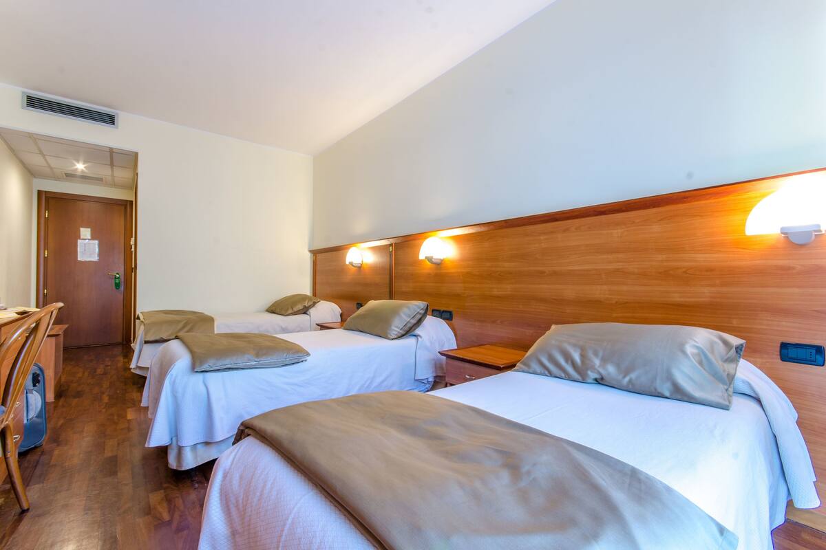 A hotel room with two single beds, a wooden headboard, a desk, and a chair.