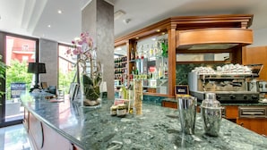A hotel bar with a marble countertop, various bottles, a coffee machine, and a decorative orchid plant. - Hotel Federico II (L'Aquila)