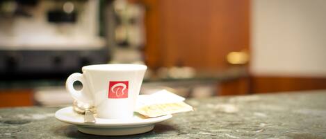 A white cup with a logo on a saucer on a marble countertop.