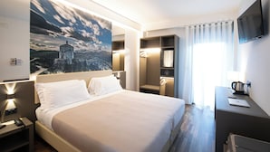 A hotel room with a large bed, bedside tables, a desk, a TV, and a painting on the wall. - Hotel Federico II (L'Aquila)