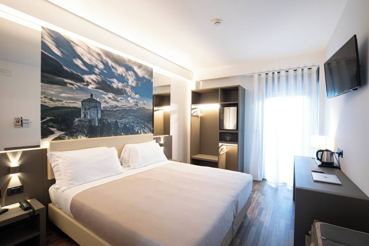 A hotel room with a large bed, bedside tables, a desk, a TV, and a painting on the wall.