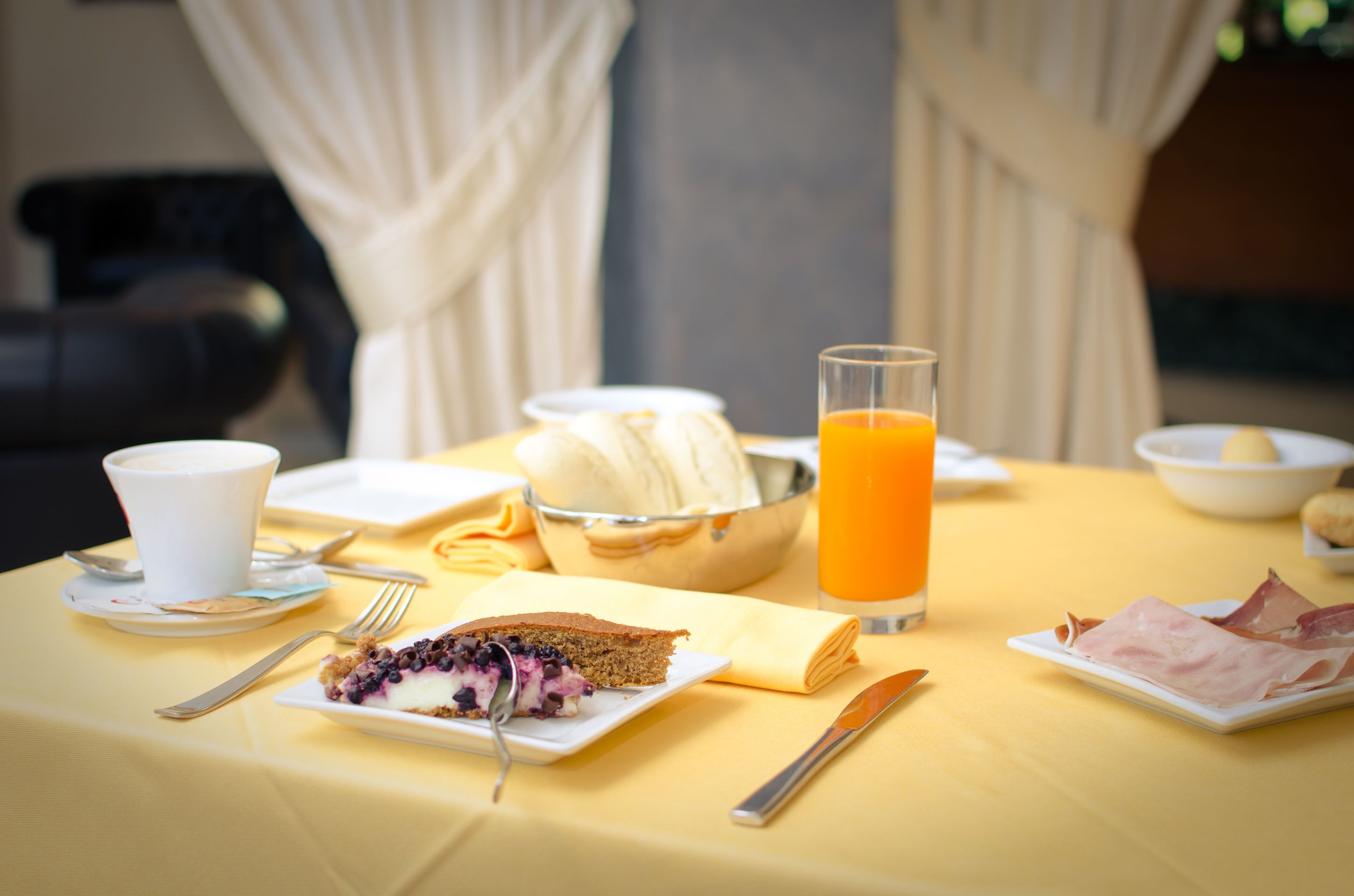 Una mesa de desayuno con una porción de pastel de arándanos, un vaso de jugo de naranja y un tazón de plátanos.