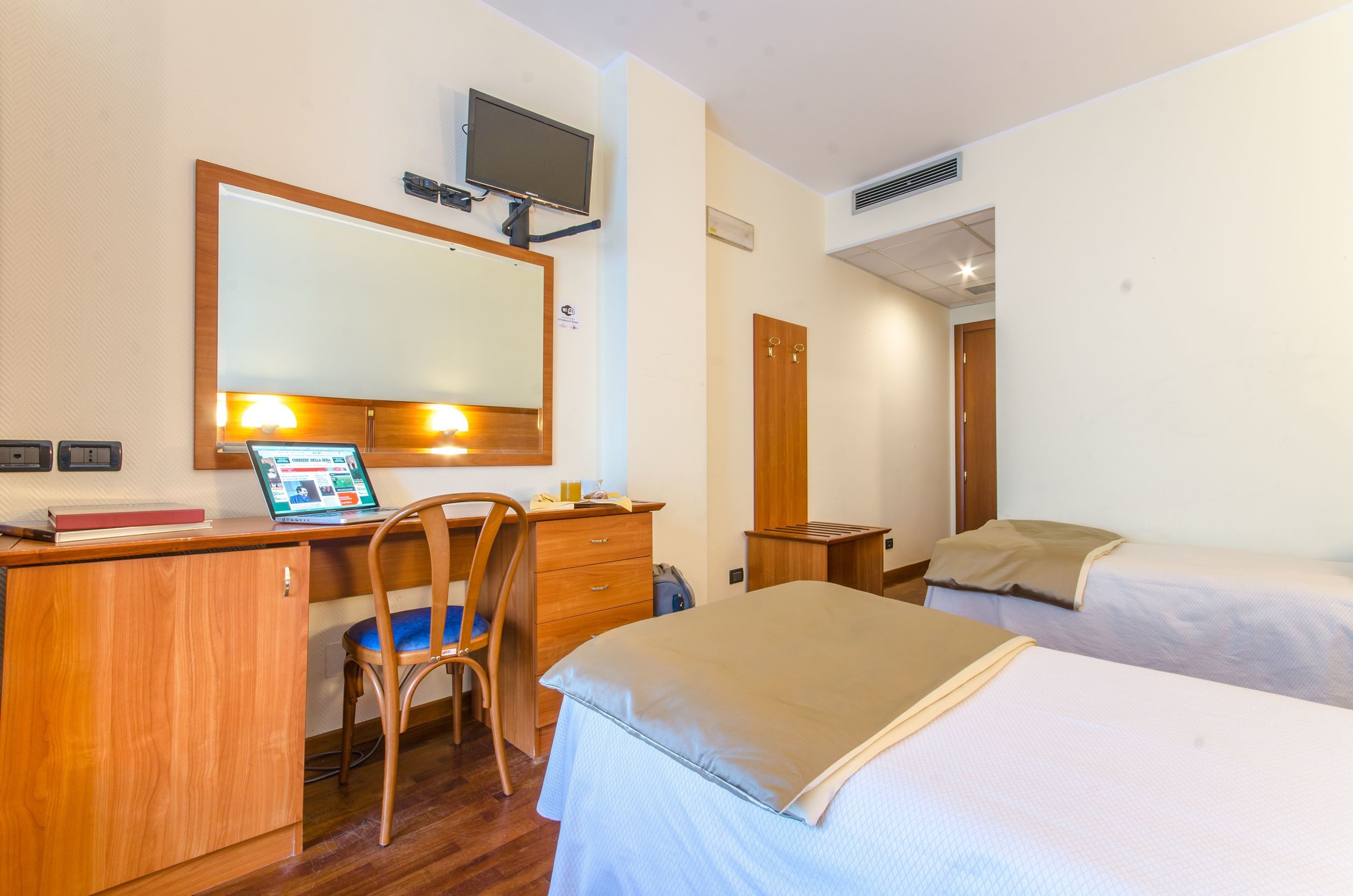 A hotel room with a desk, chair, bed, and a television mounted on the wall.