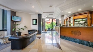 A hotel lobby with a reception desk, a leather sofa, a television, and a potted plant. - Hotel Federico II (L'Aquila)