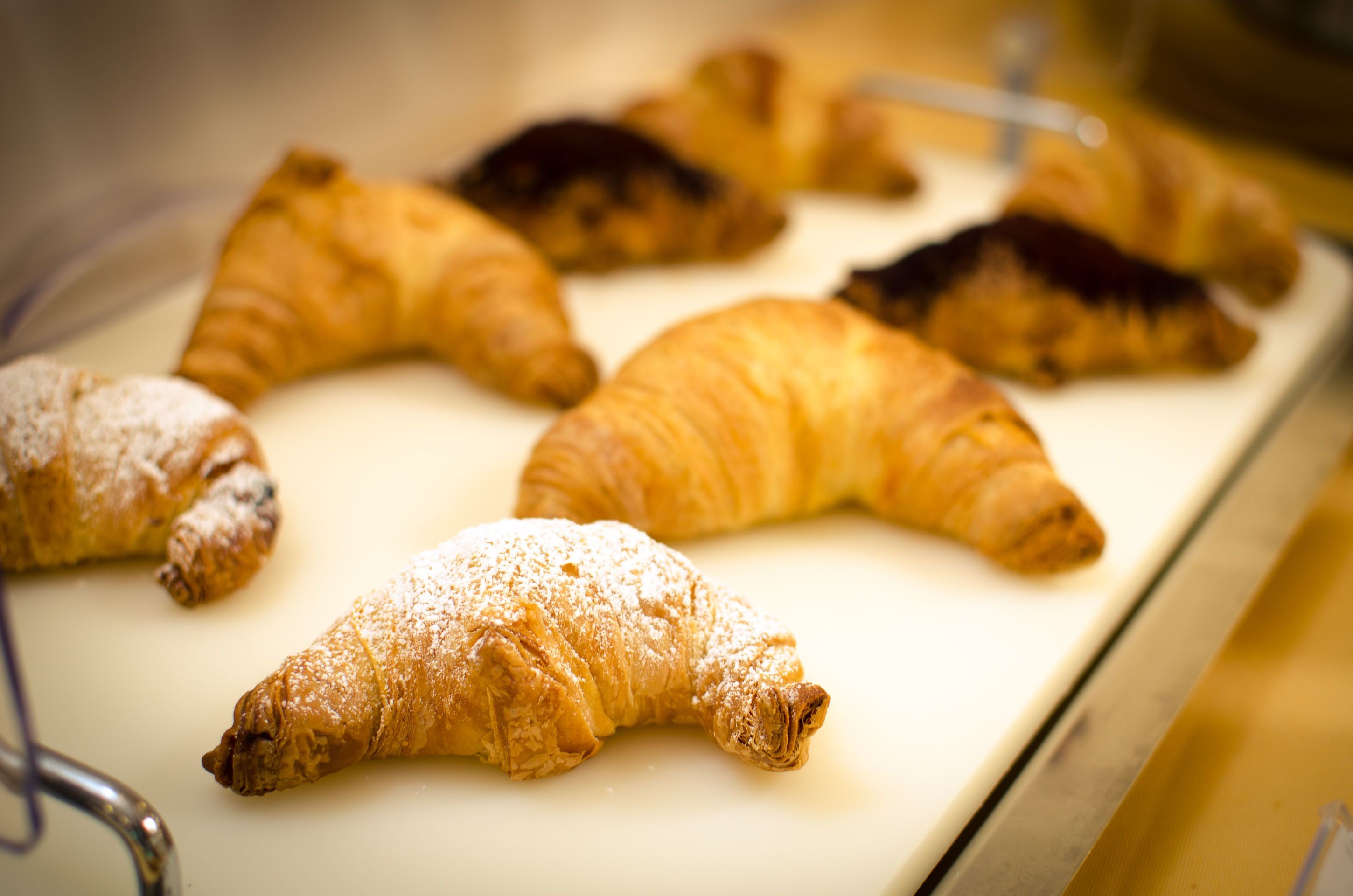 A variety of pastries, including croissants and pastries dusted with powdered sugar, displayed on a tray.
