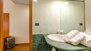 A bathroom with a sink, green marble tiles, a towel, and a suitcase.