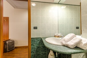 A bathroom with a sink, green marble tiles, a towel, and a suitcase.