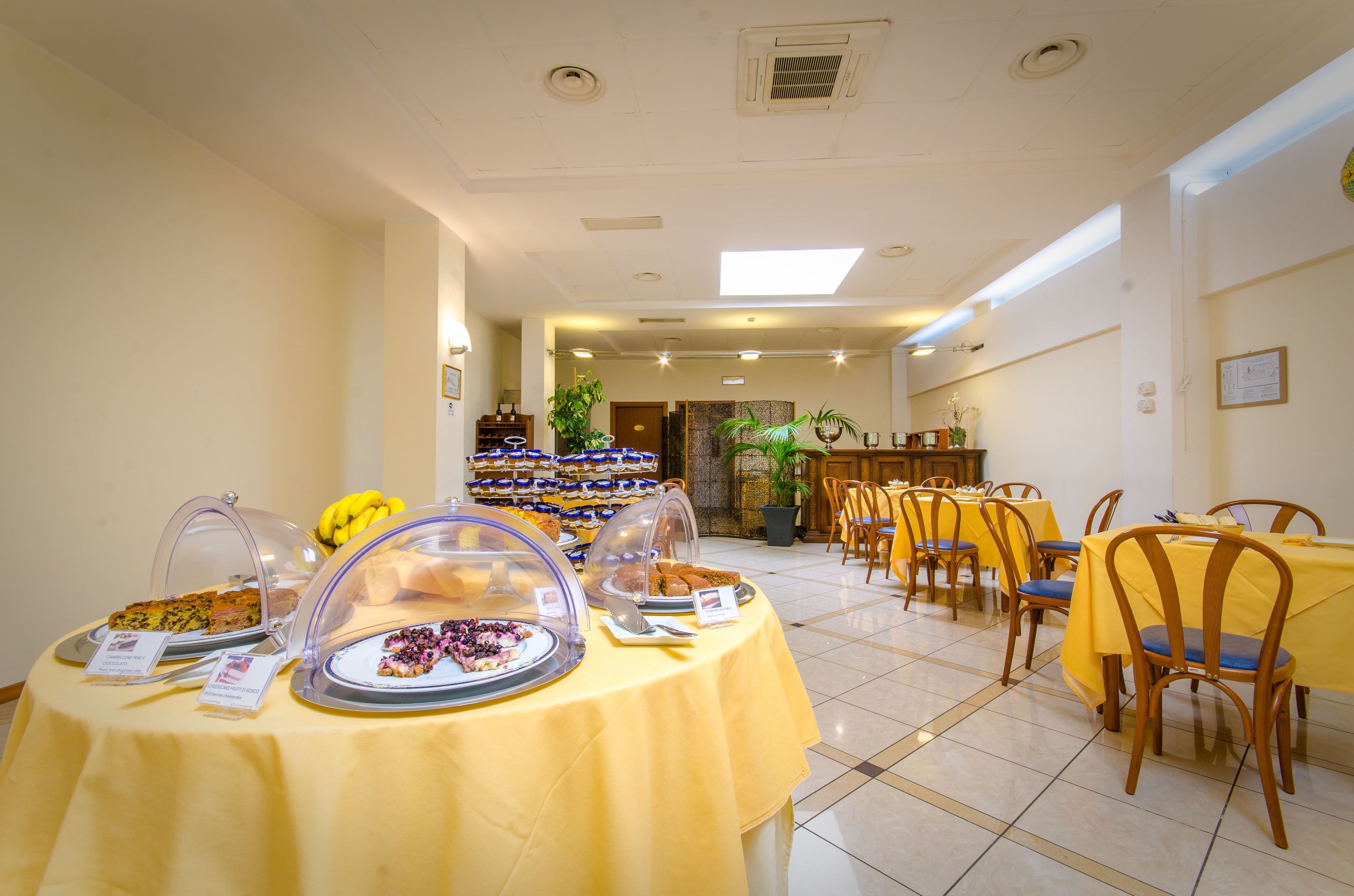 A dining area with tables covered in yellow tablecloths, surrounded by chairs.