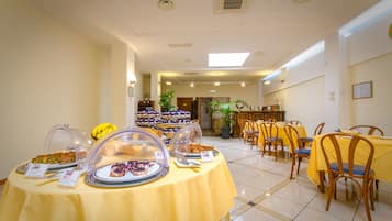 A dining area with tables covered in yellow tablecloths, surrounded by chairs.