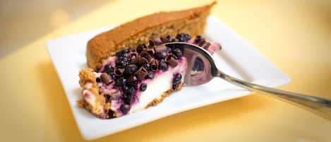 A slice of blueberry pie on a white plate with a spoon, placed on a yellow tablecloth.