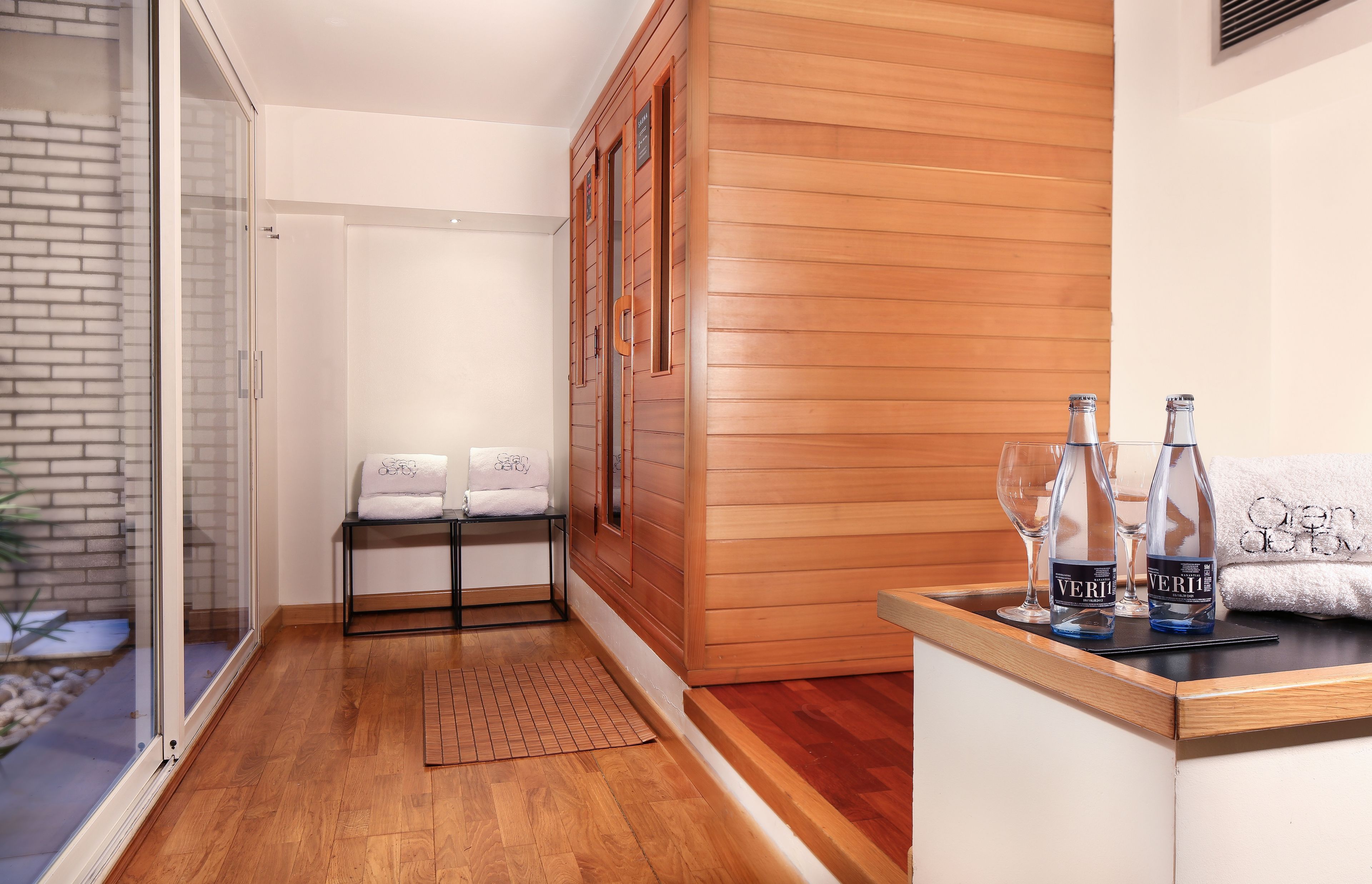 Une salle de bain moderne avec une douche en verre, un lambris en bois, un banc avec des serviettes et un comptoir avec des bouteilles.